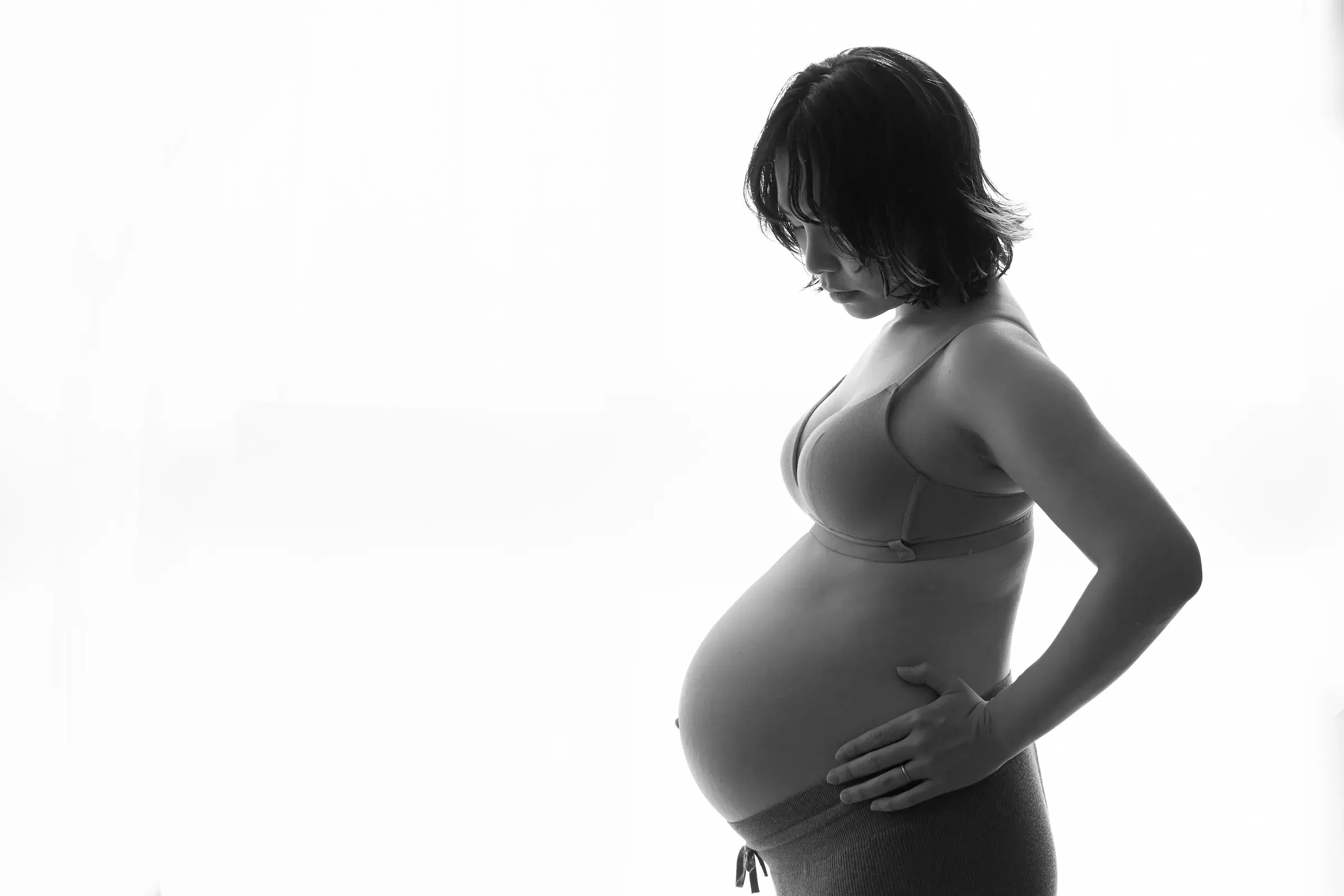 白い背景に浮かぶ、お腹に手を当てた妊婦さんの横向きシルエット