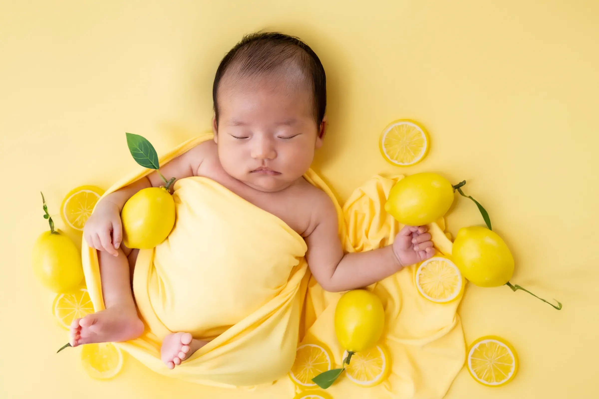 黄色い布にくるまれ、レモンに囲まれて眠る赤ちゃん