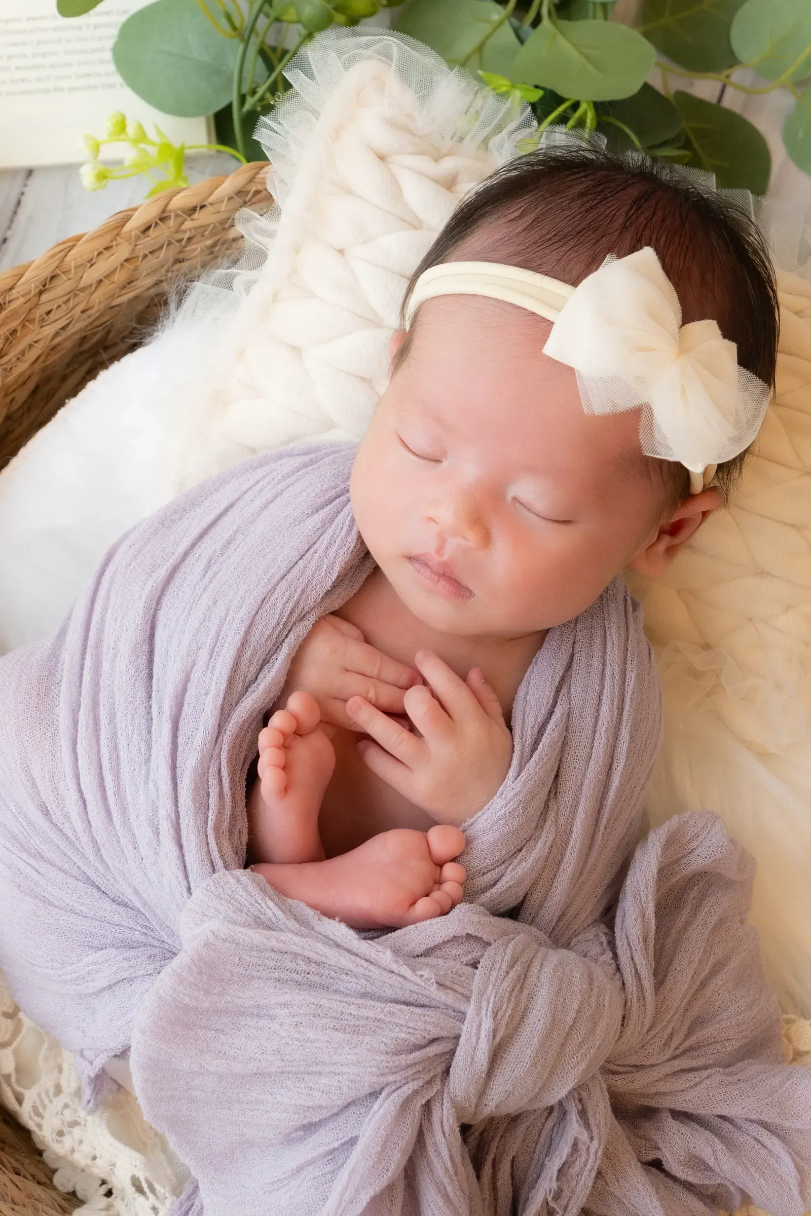 白いリボンのヘアバンドをつけ、薄紫のおくるみで眠る赤ちゃん